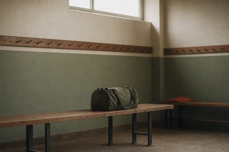 Vestiaire de stade vide et propre, un banc en bois, un sac de sport fermé, lumière de fin de journée